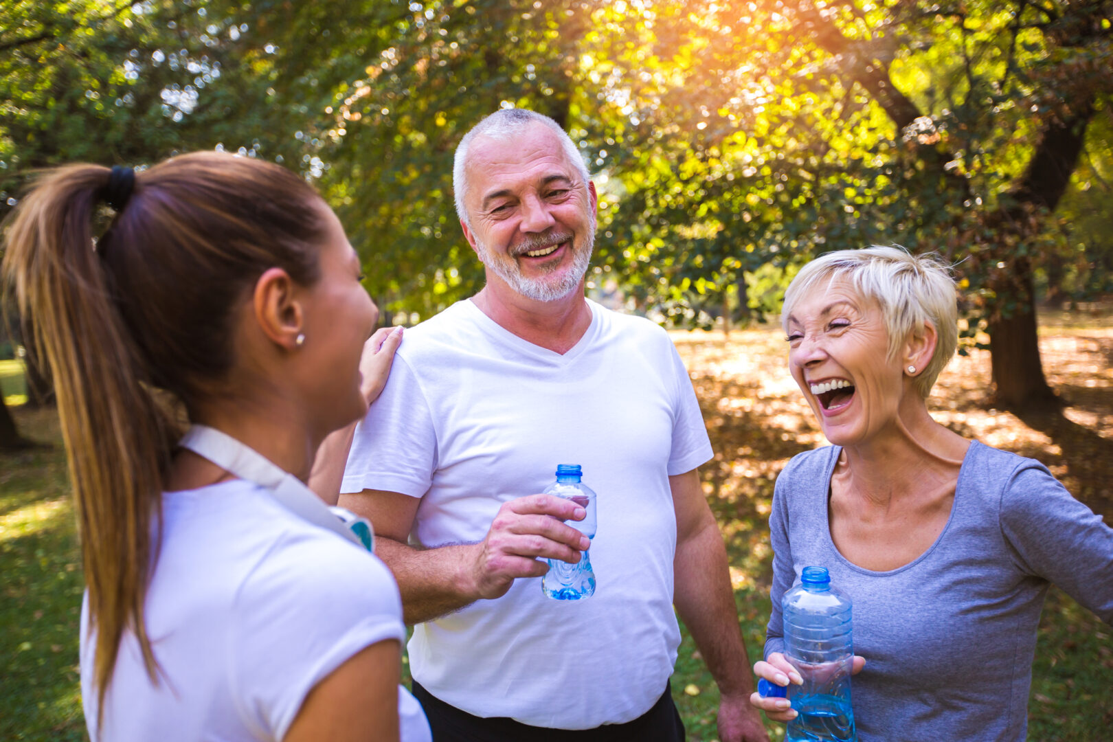 Three people laughing and drinking water in a park.